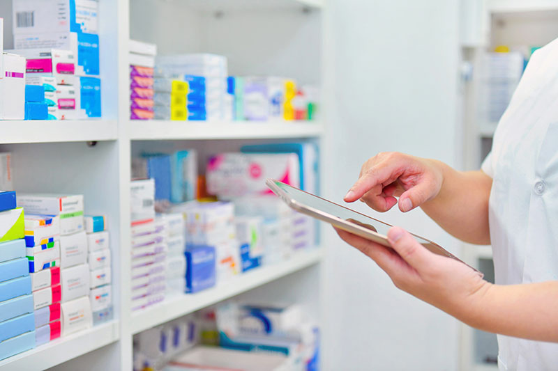 Pharmacist holding iPad in pharmacy while looking at a shelf of medications