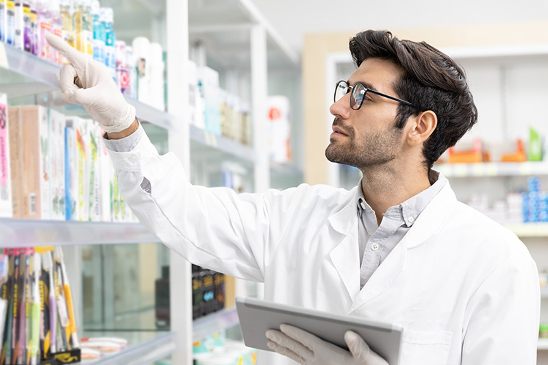 Male pharmacist checking stock drugstore using digital tablet technology in modern pharmacy